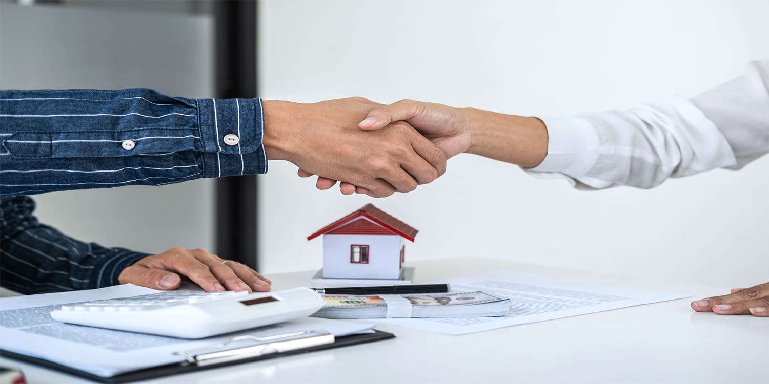 Real estate investor shaking hands with client after cash home sale agreement.